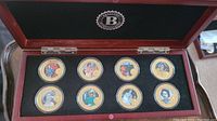 Wooden display box with 10 gold plated commemorative coins each with full-color portraits of Queen Elizabeth II from her royal tours of Canada.