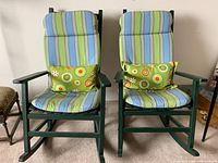 Front view of two green painted wooden rocking chairs with striped cushions and green patterned bolsters.