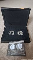 Black display case holding two commemorative silver coins and certificate