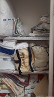 Shelf with white duvet, folded linens, towels and crocheted blanket in plastic bag
