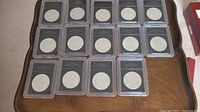 Overview of fifteen slabbed coins arranged in rows on wooden surface