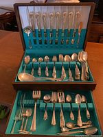Photo of open wooden flatware canteen showing the arranged silver plated flatware including knives, forks, spoons, and specialty pieces.