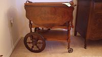 Side view of the wooden tea trolley showing drop leaf raised and large spoked wheel.