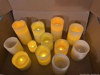 Photo showcasing 12 battery operated candles of varying sizes, glowing with warm yellow light inside a box.