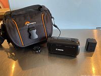 Photo of Canon video camera, battery, and Lowepro camera case displayed on a surface.