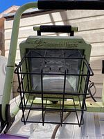 Front view of one Commercial Electric LED flood light with protective metal cage and handle.