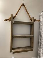 Full view of the wooden hanging shelf showing three shelves and thick rope hanging system