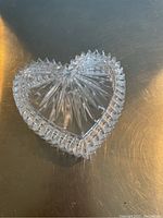 Clear heart shaped glass dish base with starburst interior pattern and scalloped edge, photographed from above on a dark surface.