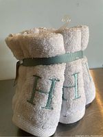 Six white wash cloths bundled with a light blue-green ribbon showing the letter H embroidered on each.