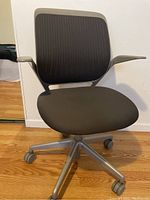 Front side view of a grey rolling office chair with black mesh backrest, padded seat, and silver base with casters.