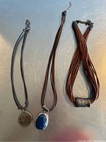 Three vintage Silpada necklaces laid flat showing pendants and leather straps on a grey surface.