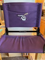 Front view of the purple stadium seat showing padded backrest with embroidered logo and padded seat area.