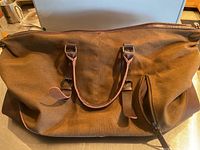 Brown canvas travel bag with leather straps shown front view on countertop