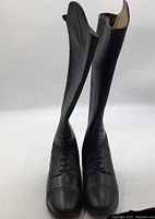 Front perspective of tall black leather riding boots showing lace-up detail and perforations on toe caps.