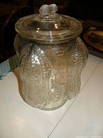 Front angled view of the clear vintage Planters Nuts jar showing embossed peanuts and lettering, with lid on top