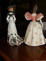 Two Lenox porcelain figurines showing back views, focusing on dress details and hats.