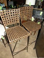 Photo showing two rattan barstools with metal frames, woven rattan seat and backrest.