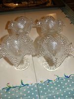Four clear cut glass sundae bowls arranged in a square, showing their ruffled petal-like edges and textured diamond pattern on a reflective table surface.