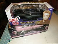 Image showing both die cast cars in original packaging stacked together, Elvis Presley Pink Cadillac in pink and James Dean Mercury Coupe in black.