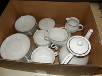 Box with teapot, cream pitcher, sugar bowl, multiple cups, saucers, and snack plates. White porcelain with silver trim.