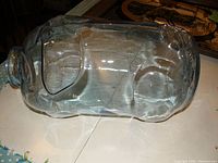 Side view of clear glass pig-shaped container showing its length and detailed molding.