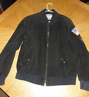 Front view of black suede and leather jacket with American flag patch on left sleeve, zip front, ribbed cuffs and waistband.
