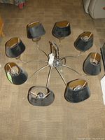 Overhead view of mid-century modern chandelier showing eight black lamp shades attached to curved metal arms.