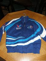 Front view of the blue NASCAR Mark Martin Valvoline Racing jacket on a wooden table showing logos and zip-up front.