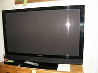 Front view of the Pioneer 50-inch TV on a wooden stand showing the screen turned off with remote and soundbar below.