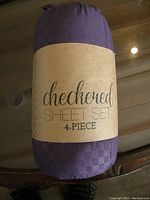 Rolled and packaged purple checkered sheet set with a brown paper label reading 'checkered sheet set 4-piece'.