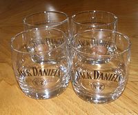 Four clear glass tumblers with Jack Daniels Old No. 7 logo arranged on a wooden surface.
