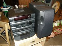Photo showing Sony multi-component stereo system with two large black speakers on a wooden table surrounded by various household items.