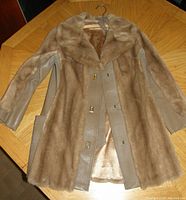 Full view of vintage dubrowsky & joseph faux fur coat lying flat showing beige faux fur trim and taupe leather-look panels.
