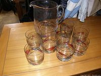 Photo showing a clear glass pitcher and eight matching glass tumblers arranged on a wooden table under indoor lighting.