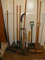 Photo showing multiple gardening tools including rakes, a manual edger, and an electric hedge trimmer with wooden handles.
