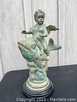 Front view of cast metal cherub riding a fish on round base