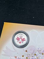 Close-up of the 2009 Royal Canadian Mint commemorative coin showing the design of two doves with hearts and a bow in protective capsule and partial view of surrounding packaging.