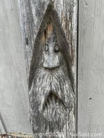 Close-up image of the hand carved face and figure detail on the weathered wooden post.