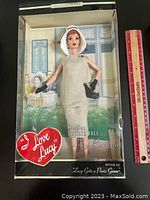 Front view of the boxed collectible doll in costume with ruler for scale.