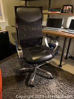Front view of black professional desk chair showing padded seat, mesh backrest, headrest, and silver armrests.