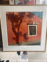 Framed photograph showing red wall with tree shadow and a window.