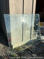 Clear tempered glass table top leaning against a wall outdoors, showing transparency and square shape.