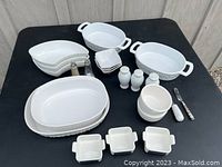 White porcelain serving dishes including various bowls, salt and pepper shakers, small appetizer and condiment dishes displayed on a black surface against a wood background.