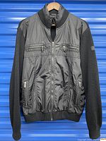 Full front view of black Paul & Shark Yachting jacket with nylon body and wool knit sleeves and collar, zipped up on hanger.