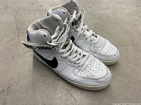Left side view showing white leather high top with black Nike swoosh and Supreme branded strap around ankle.
