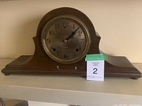 Front view of the antique wooden mantel clock showing the clock face and base.