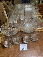 Wide view of assorted clear crystal glassware on wooden surface including bowls, glasses, and a lidded jar.