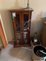 Closed wooden display case with glass doors on front showing DVDs inside, with silver-colored handles and a lamp on top.