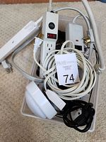 Top view of bin containing white and black power strips, white extension cords, a white multi-outlet power strip with switch, and various cables bundled together.
