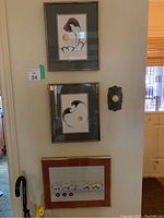 Three framed art prints hung on a wall, two vertically aligned one above the other and a third below them with different framing and matting.